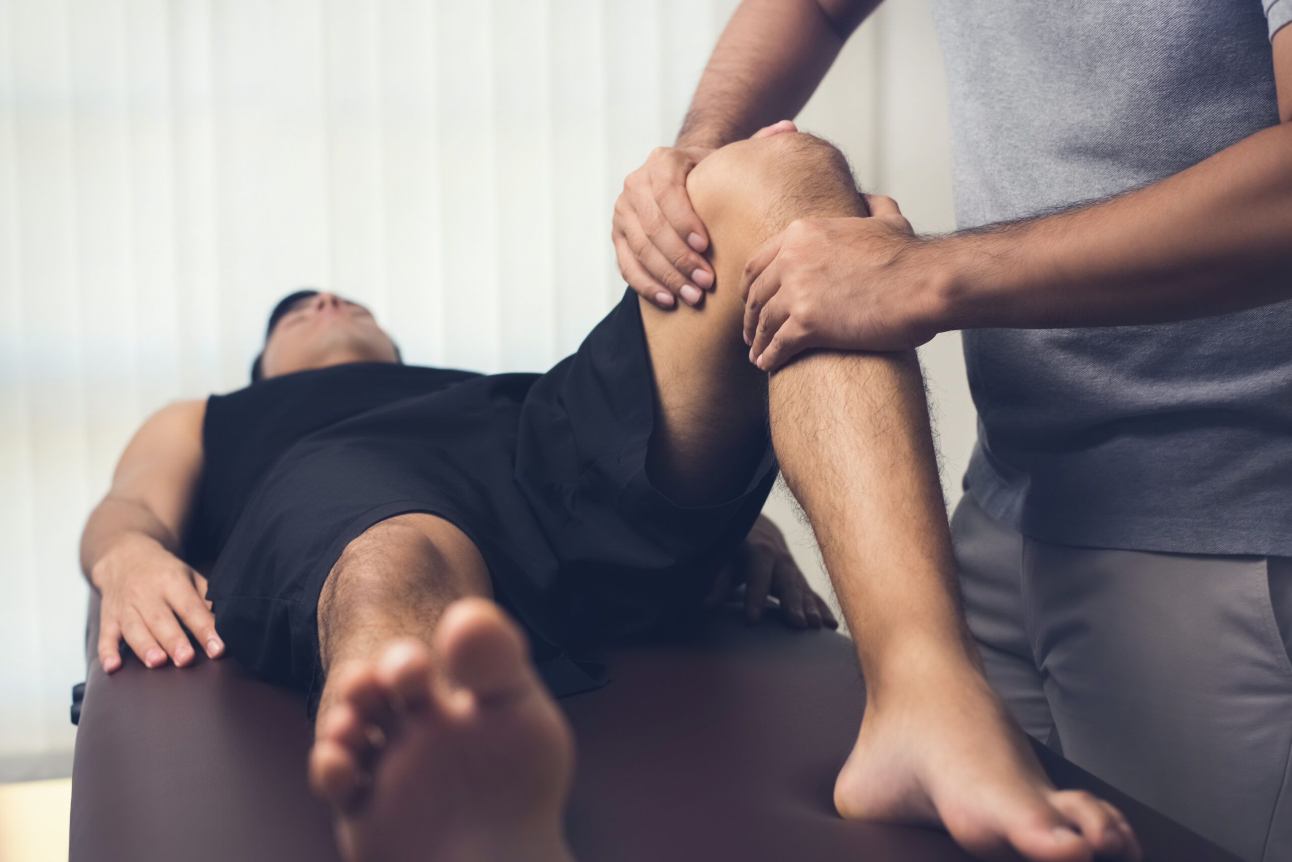 Male physical therapist working on the knee of athlete patient in a professional physical therapy clinic