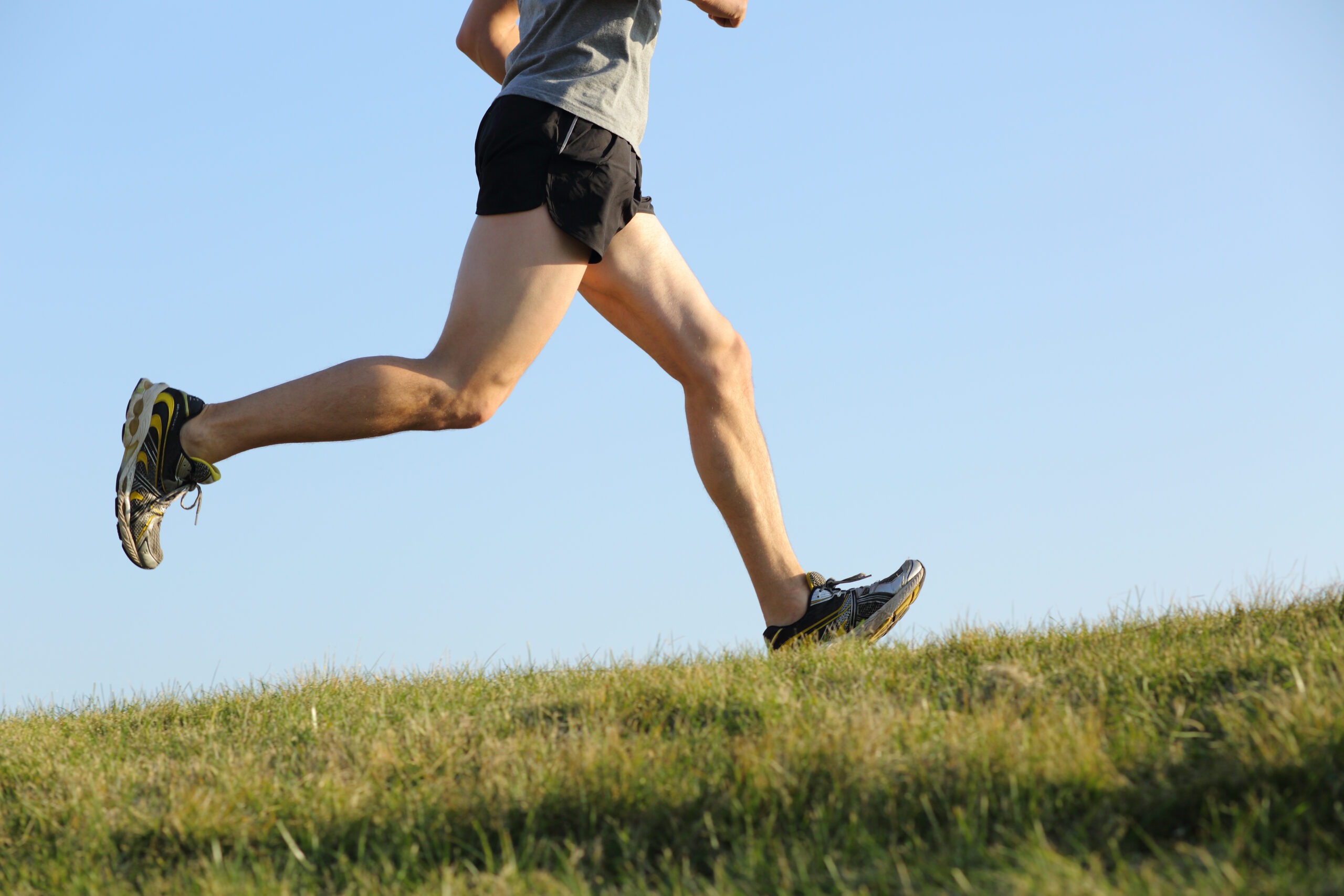 Side view of a jogger legs running on the grass with the horizon in the background