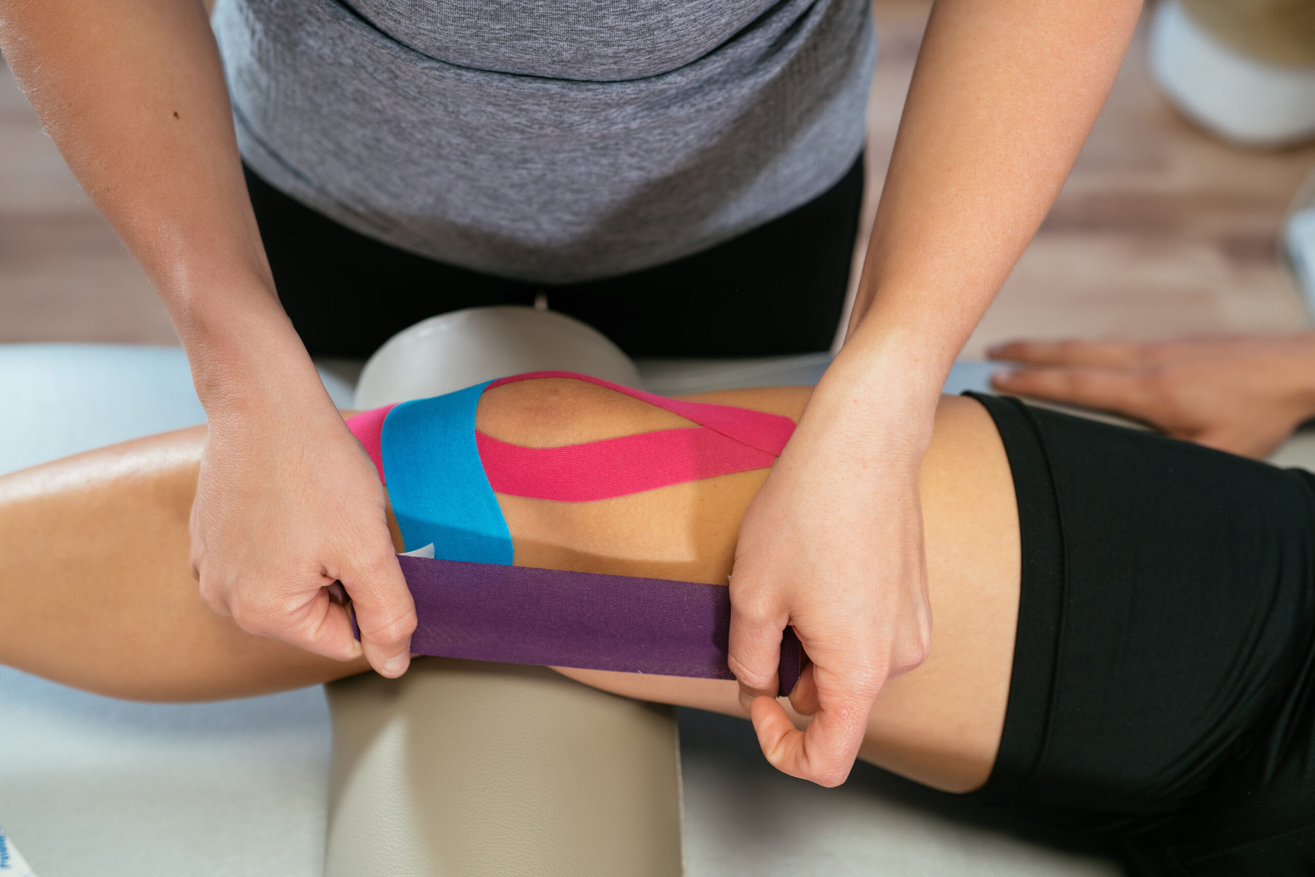 Photo detail of the hands of a physical therapist applying K tape to a patient's knee showing why K tape works