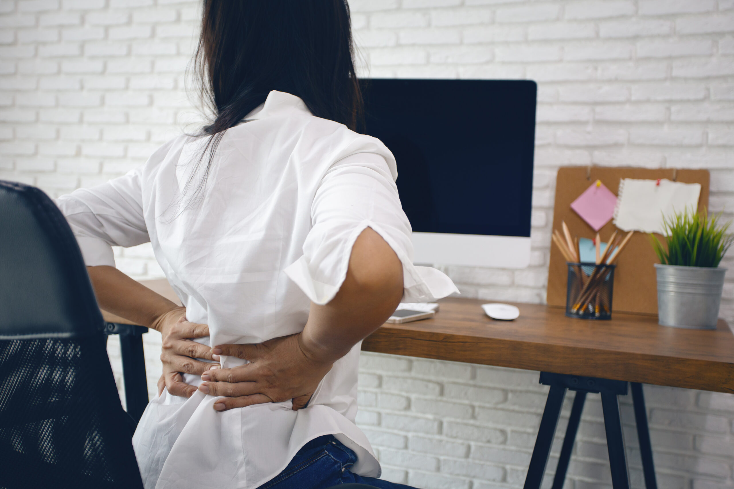 woman sitting at work desk with back pain