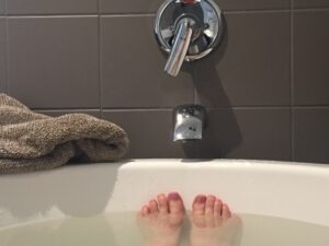 photo from the perspective of someone soaking in a bathtub. view is of a person's toes poking up above the surface of a full bathtub for a soaking in epsom salt